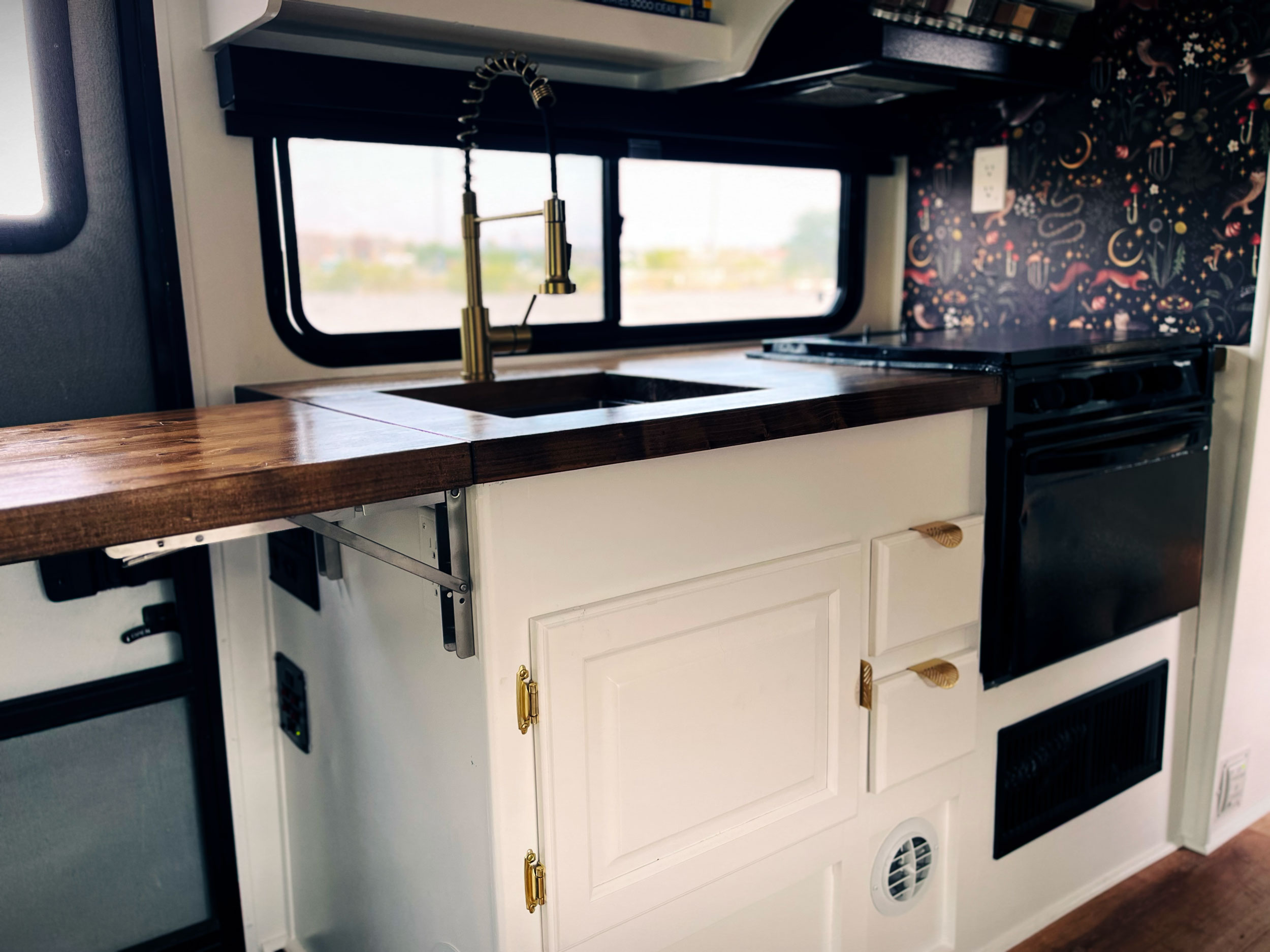 RV kitchen interior with white cabinets, wooden countertops, gold faucet, and stove.