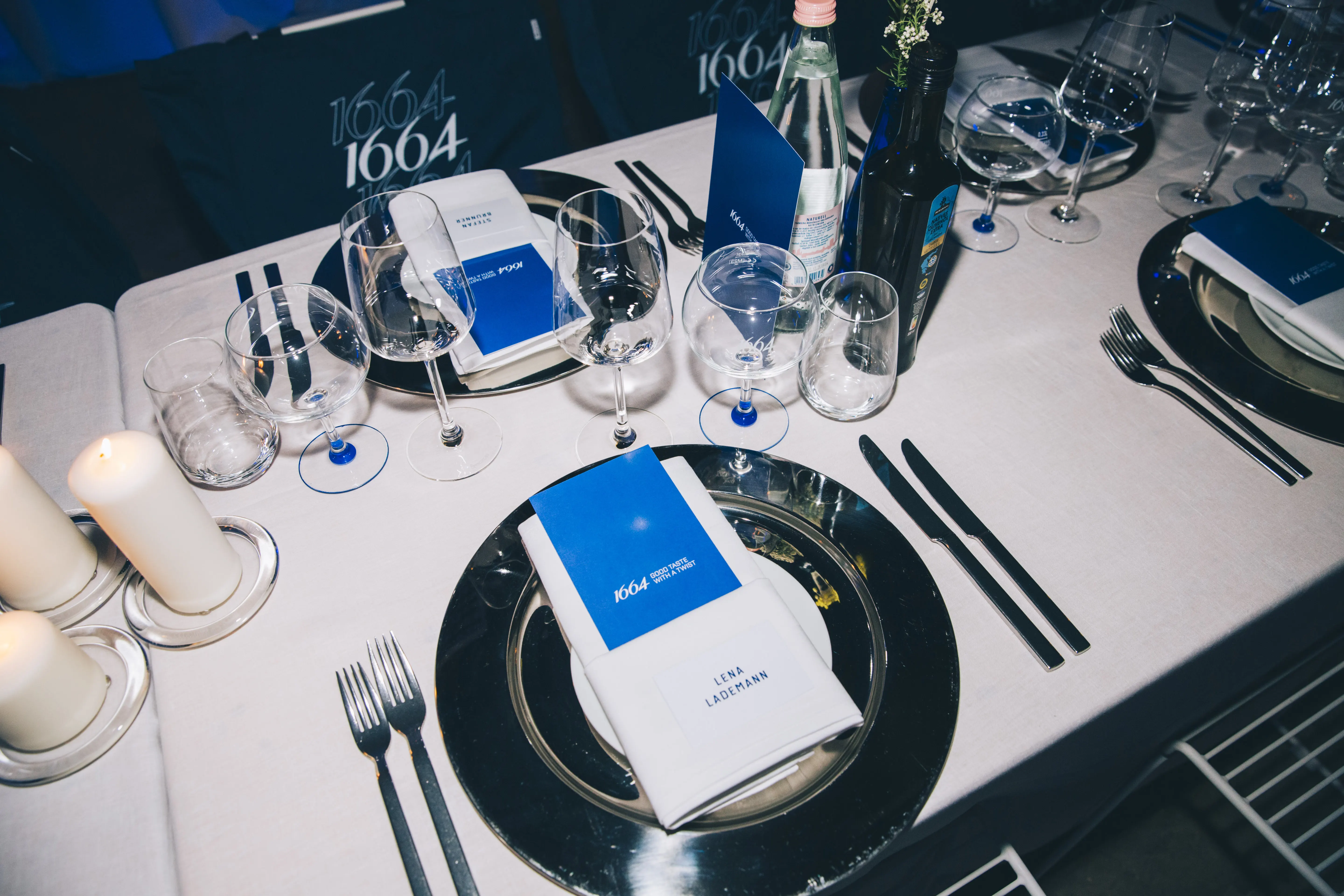Festive place setting with silver charger plates, menu cards, candles and blue 1664 accents.