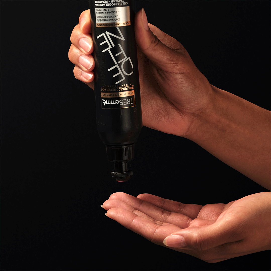 A hand holds a black bottle, pouring a liquid into the palm of another hand against a dark background.