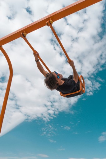 girl in black shirt and blue denim jeans riding on orange swing under blue and white