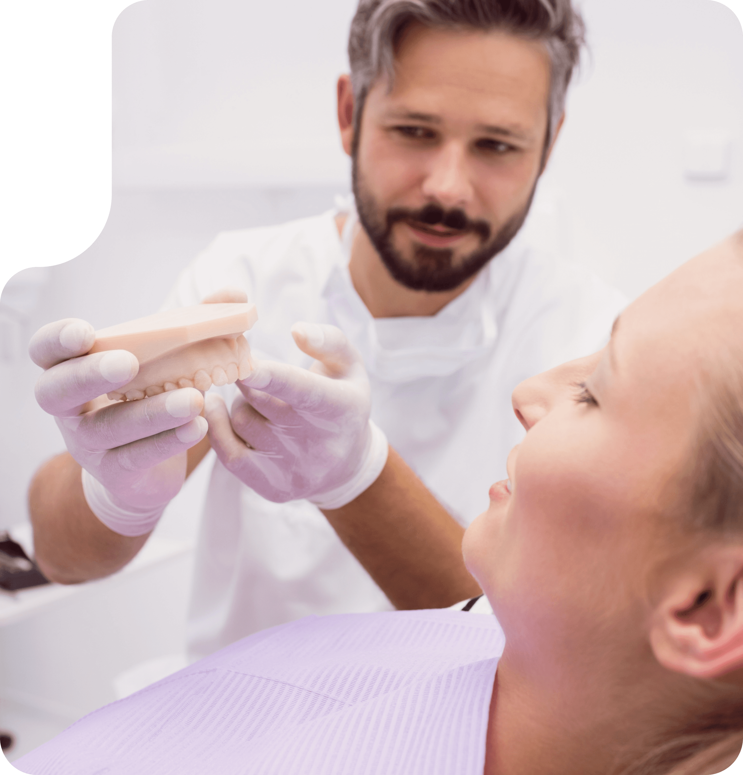 A dentist holding a dental model and explaining the dental crown procedure to a patient lying in the dental chair.