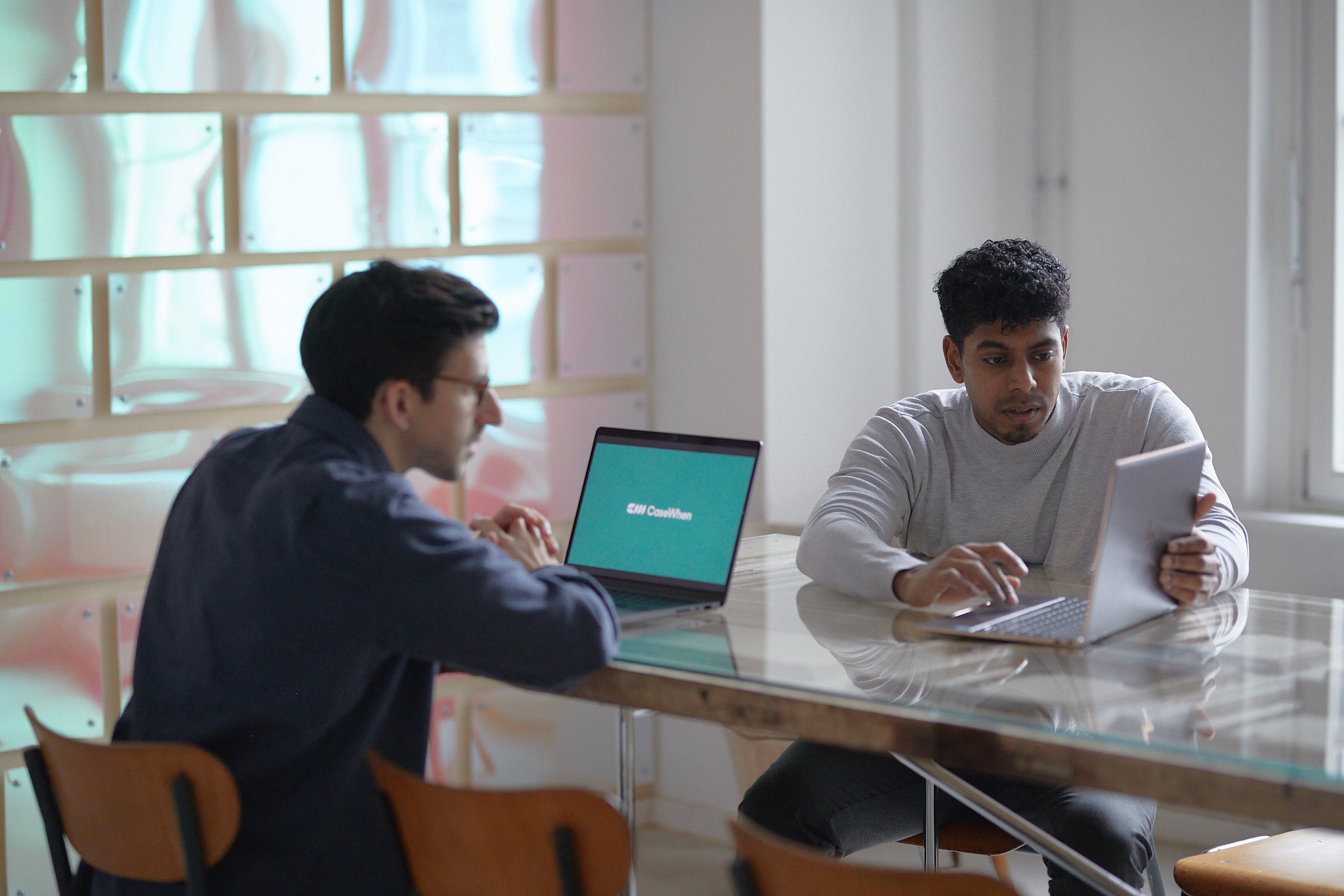 CaseWhen Consulting founders, Sajagan Thirugnanam and Austin Levine, collaborating on Power BI consulting strategies in a modern workspace with laptops displaying the CaseWhen Consulting logo.