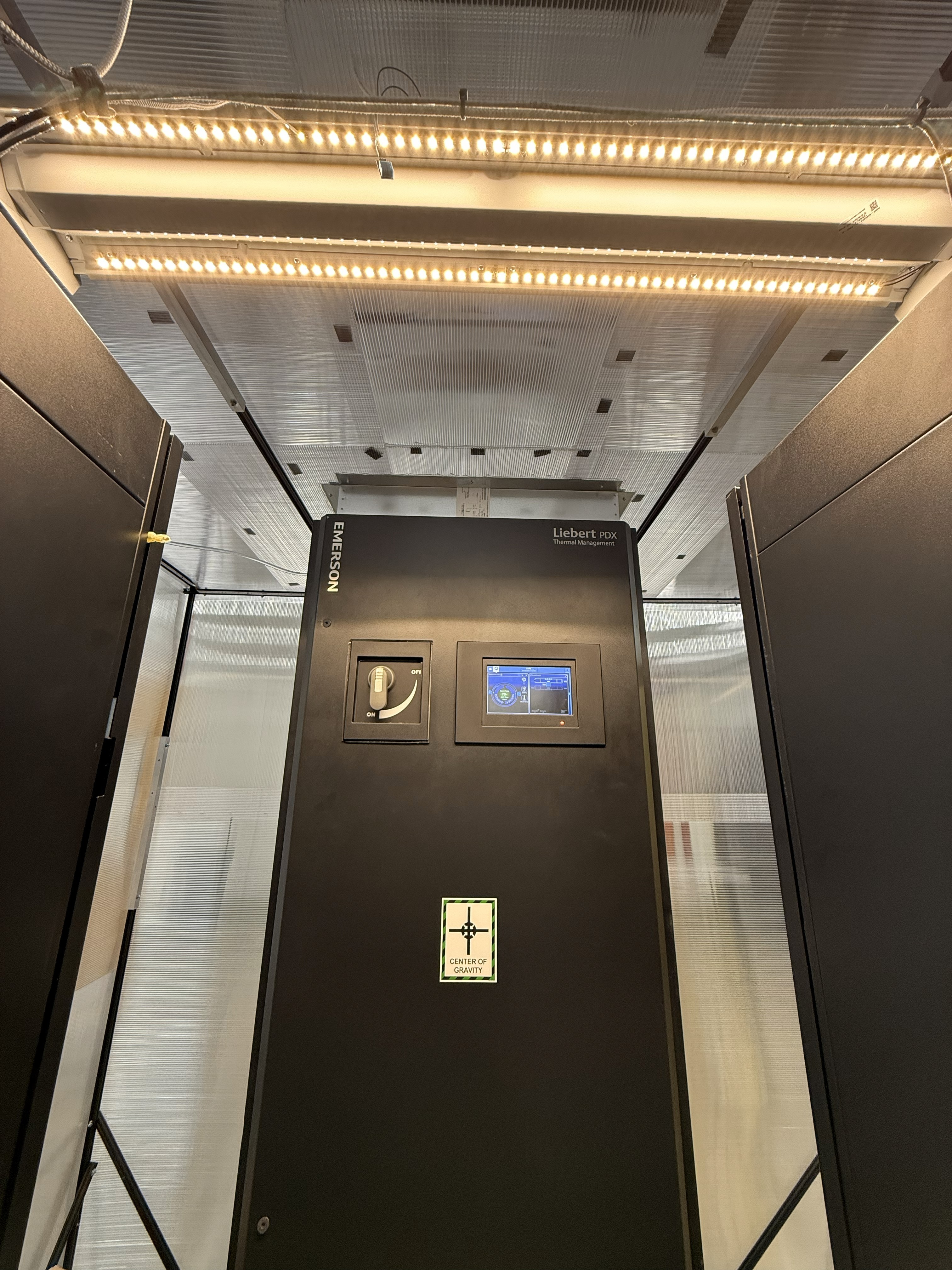 FLUIX data center lab - includes a computer room air conditioning unit with a bottom supply air discharge and a top-mounted hot air return sensor. The unit is remotely operated by a local server.