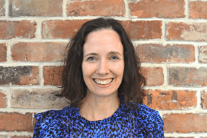 Person smiling and holding a brick wall in front of them.