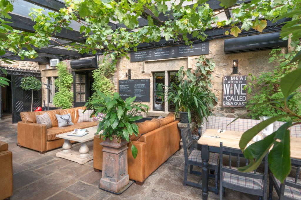 Elegant outdoor terrace with leather sofas under plant-covered pergola, lush green garden restaurant seating area with tropical vibe
