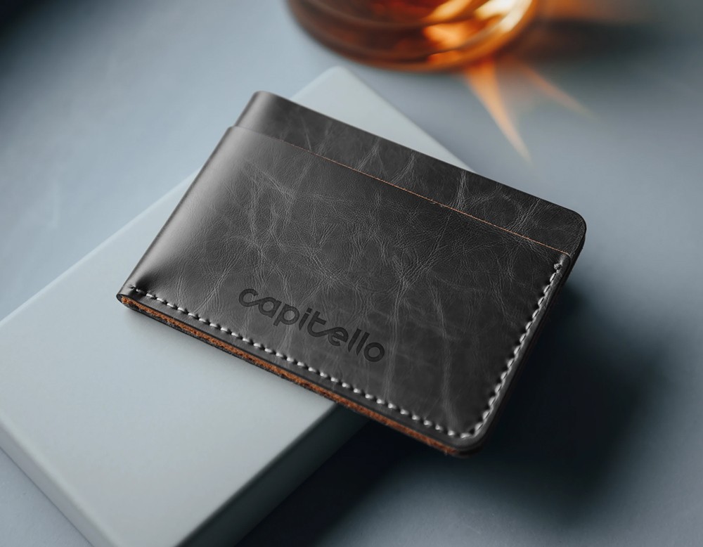 A dark leather bifold wallet placed on a dark textured surface, used as a brand collateral mockup in the Capitello Finans identity system.