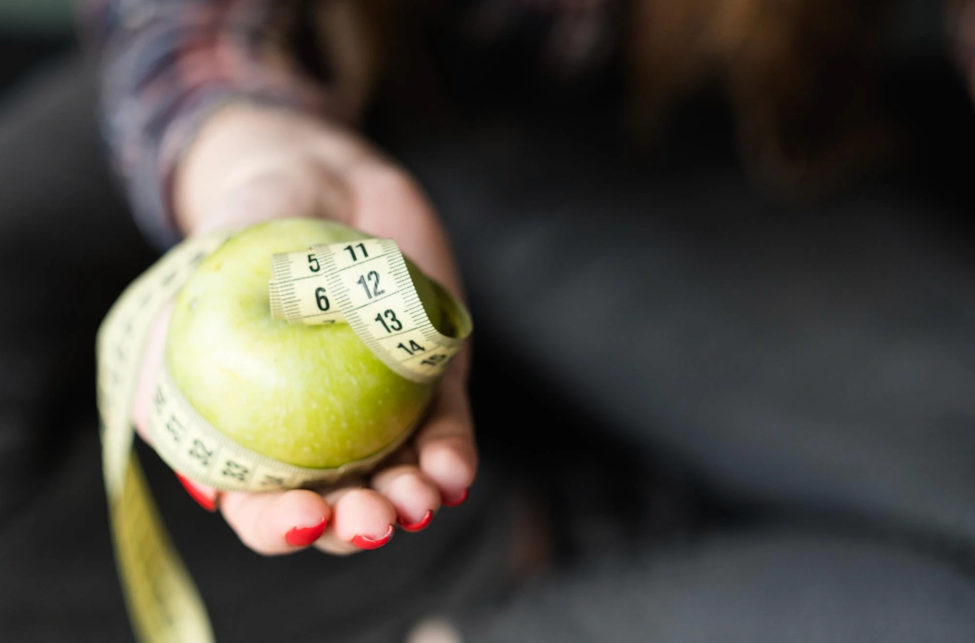 Hand holding a tape measure wrapped around an apple, illustrating smarter fitness tracking with the Caloric app