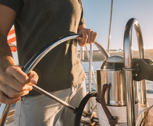 Sail Boat Steering wheel with a man driving behind it. close up shot of shiny aluminum metal work