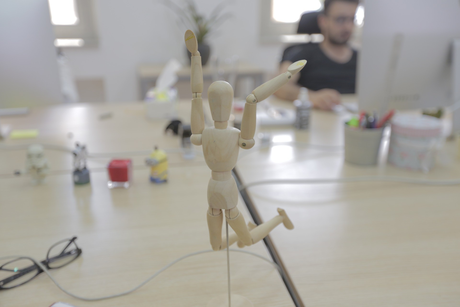 Wooden artist mannequin posing on a shared desk in Plexable's Amman office