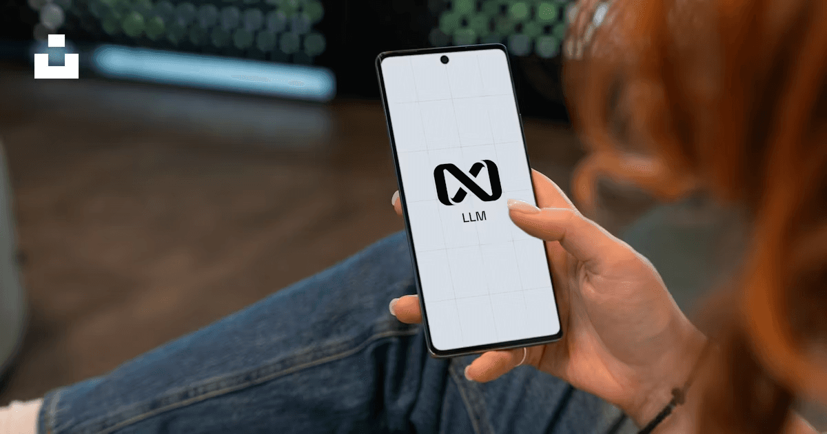 A close-up of someone holding a smartphone that displays an “LLM” logo on a clean white screen, with a blurred background. It suggests large language models and AI tools moving into everyday workflows and professional tasks.