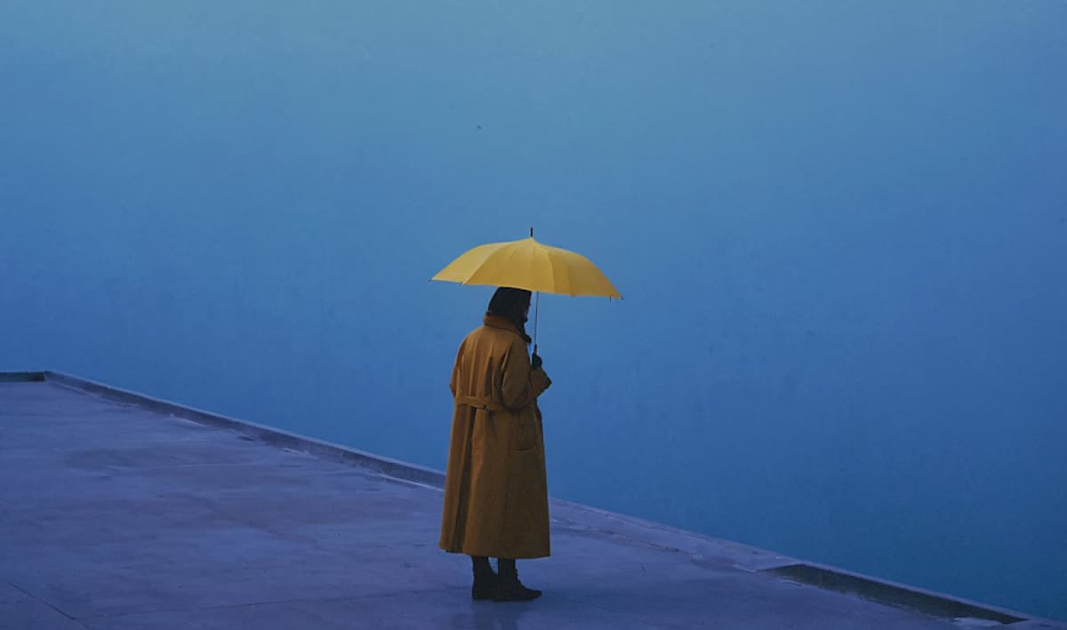 Woman stands alone against the blue background standing under a yellow umbrella
