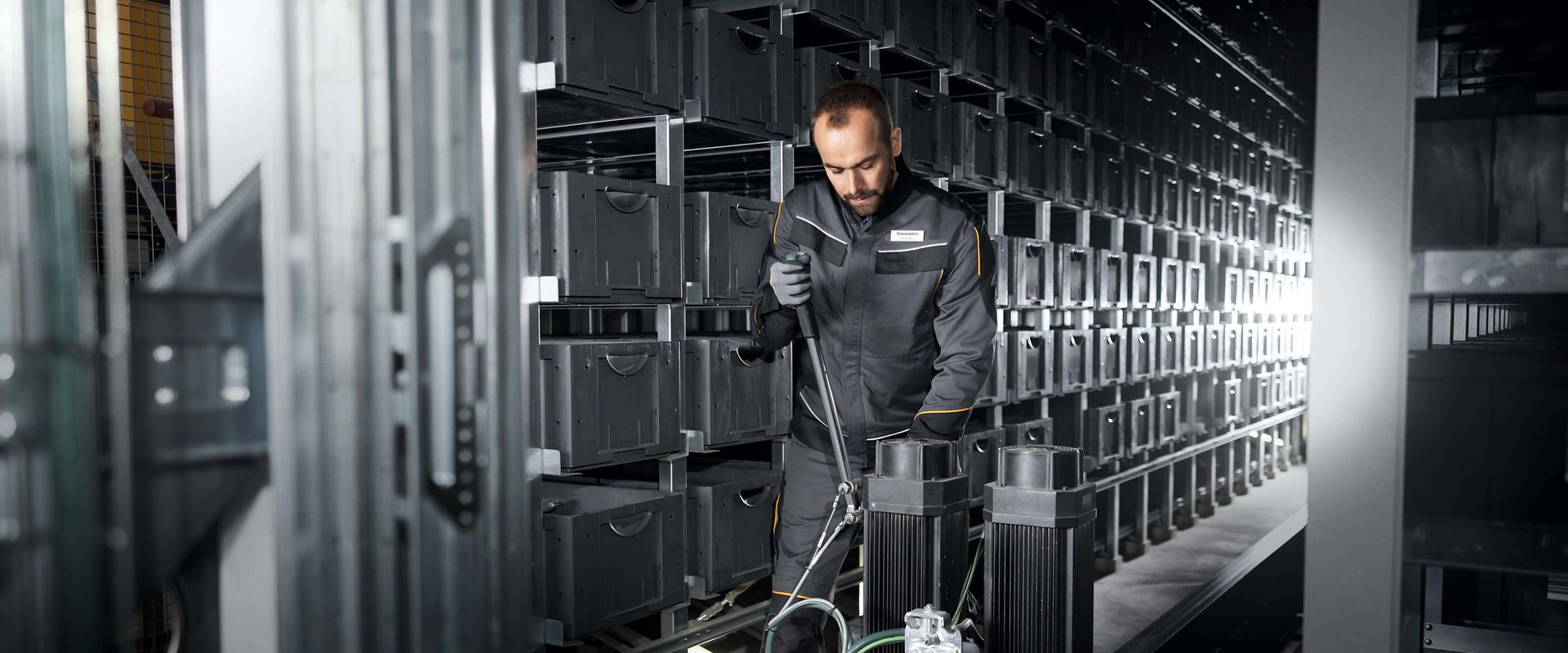 Two people in a workshop, one standing and smiling while the other leans over a car, working on it.