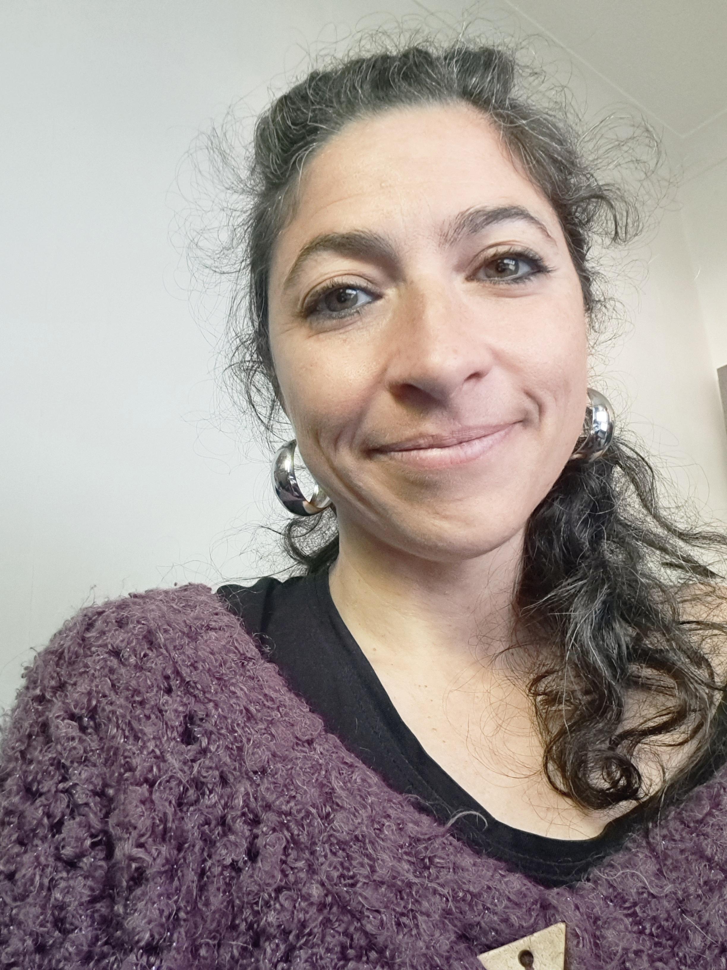 Person wearing a textured purple top with long hair pulled to one side, shown from the shoulders up.