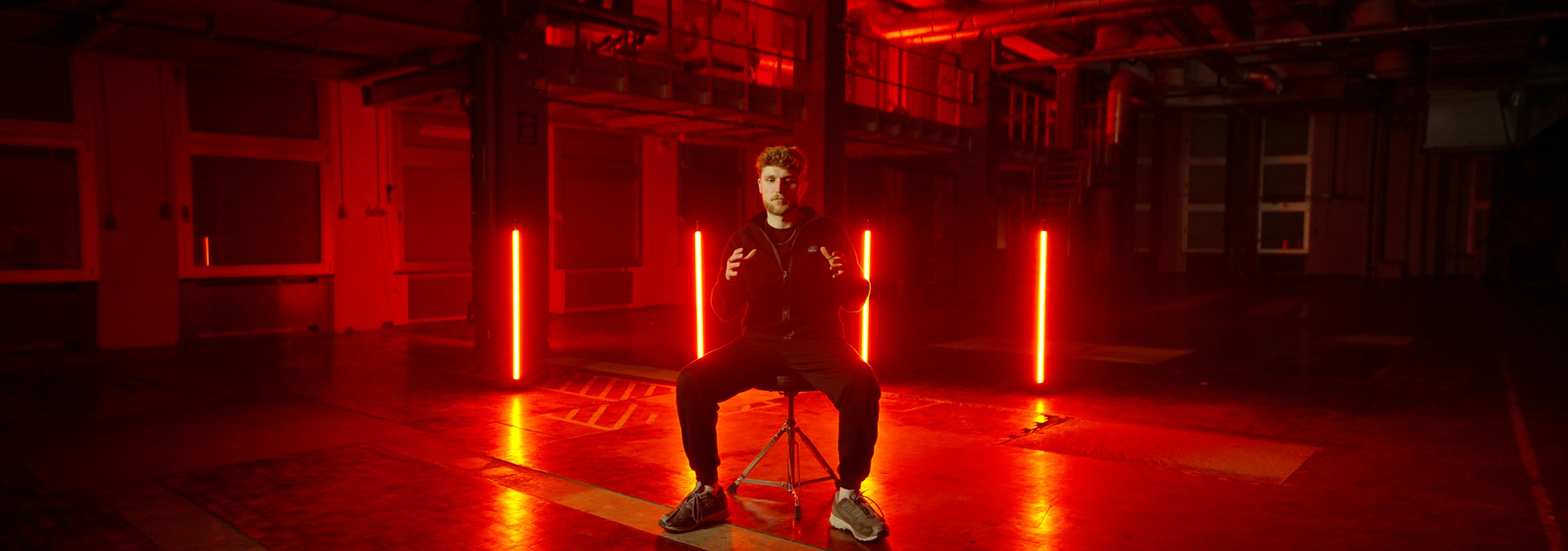 Person sitting on a stool in front of neon lights in a warehouse