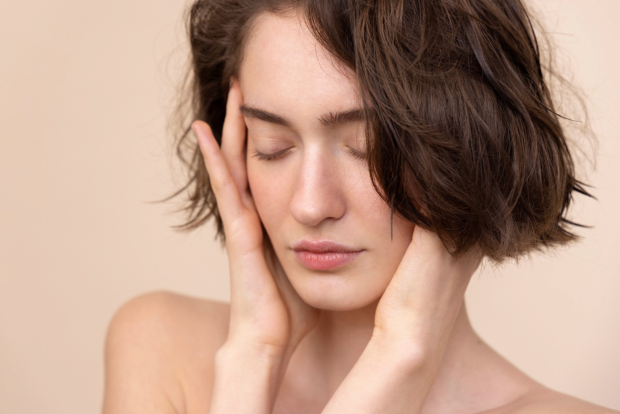 Portrait of a woman with short brown hair, eyes closed, gently holding her face