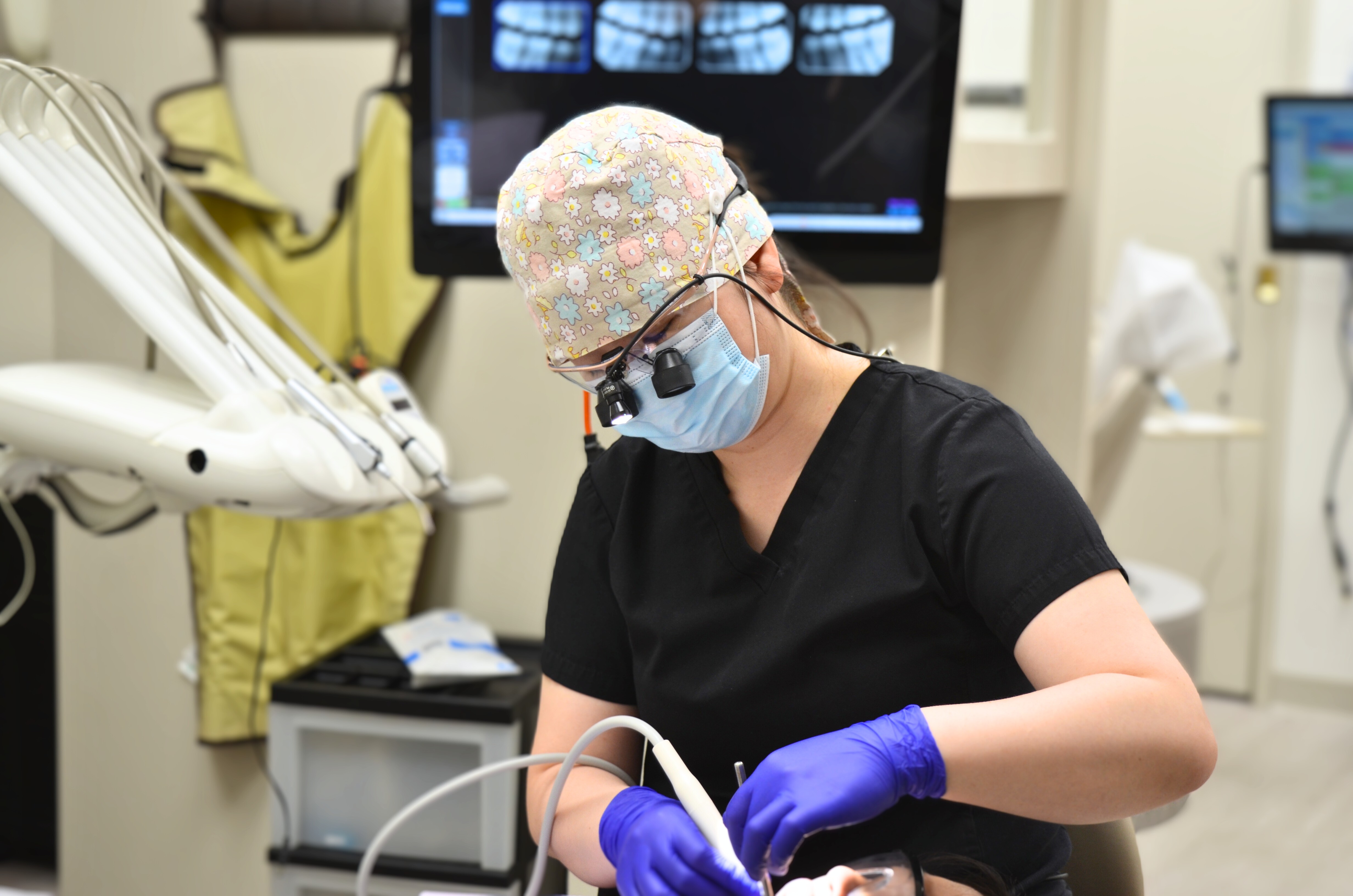 A dental professional wearing protective gear and a mask performing a dental procedure on a patient.