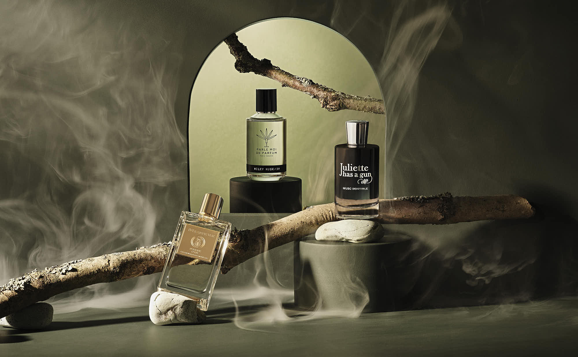 A wooden table with bottles, and sticks, and stones set against a textured wall with archway and smoke. Soft lighting creates a moody atmosphere.