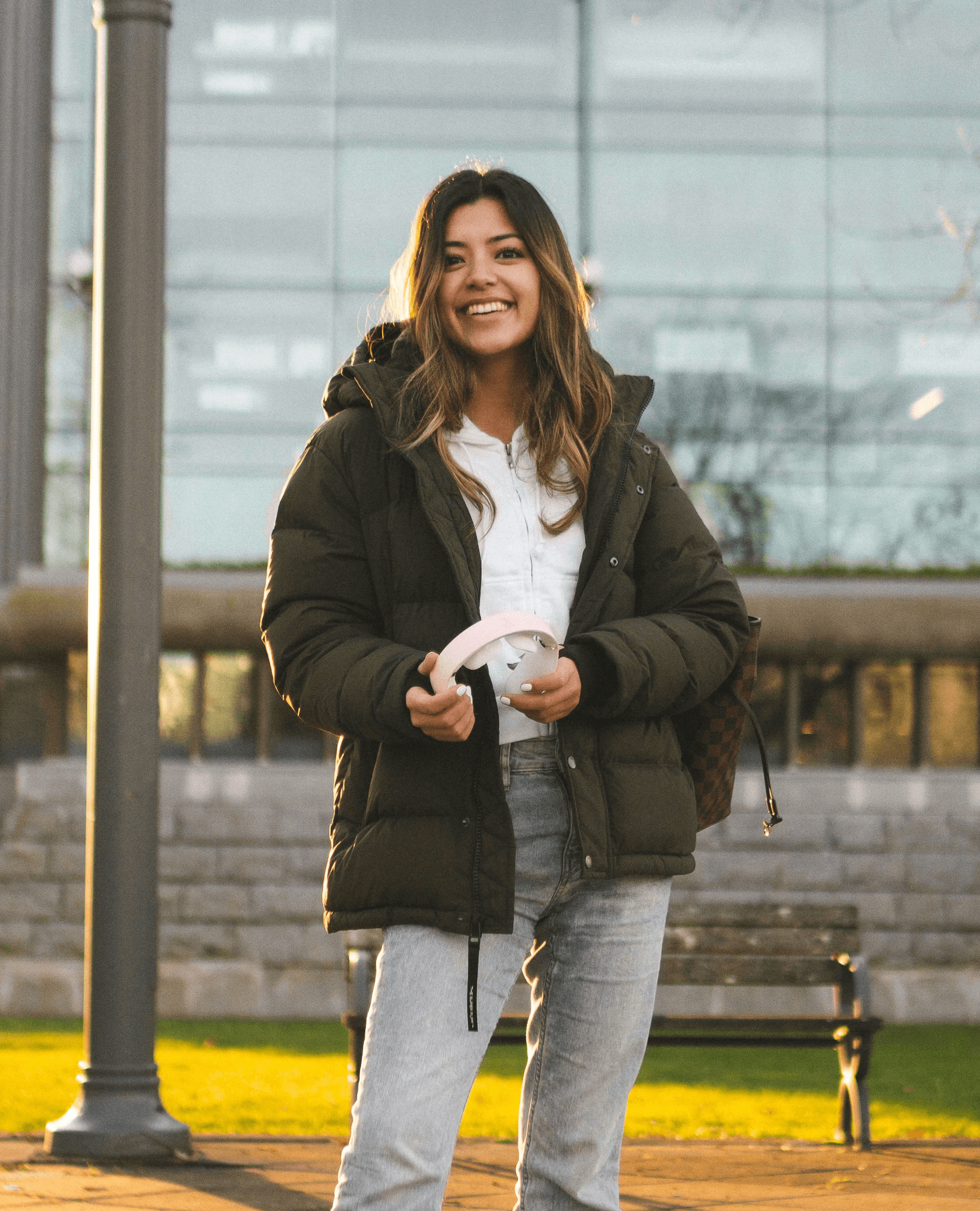 female student in gray coat and blue denim jeans sitting on bench during daytime