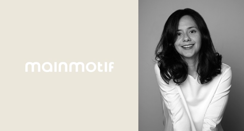 A black and white photo of a girl standing in front of a wall and smiling. Also there is some text that says: mainmotif.