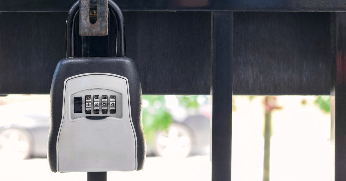 A close-up of a lockbox attached to a railing or gate. The lockbox has a four-digit code with numbers reading "1, 2, 3, and 4."