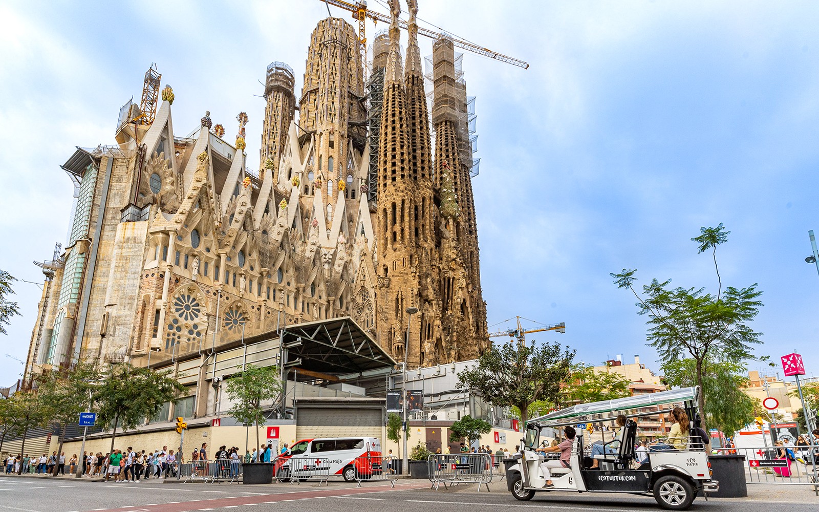 Tuk tuk driving through Barcelona streets with Sagrada Familia in the background.