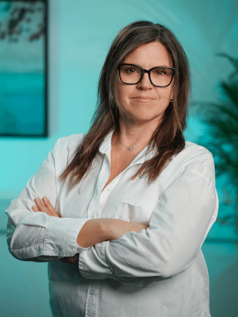 A woman with short curly hair wearing a black t-shirt looks into the camera.