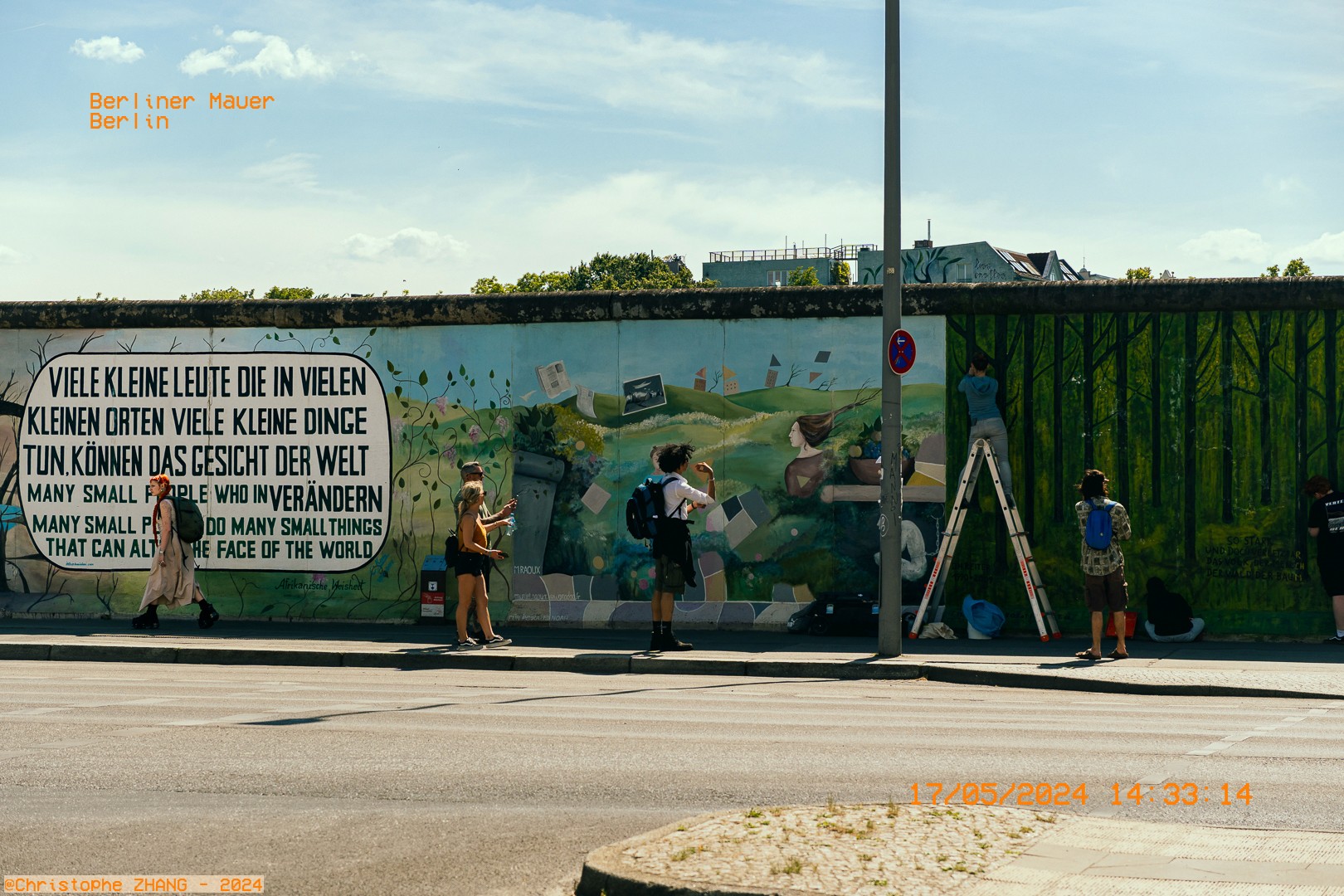 Scène urbaine au Mur de Berlin avec une œuvre d'art inspirante et des visiteurs.