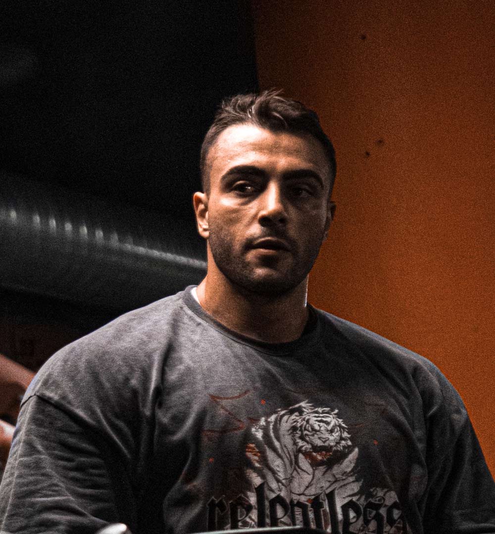 Editorial portrait of a young man with wavy hair in a knit sweater, looking over his shoulder in soft light.