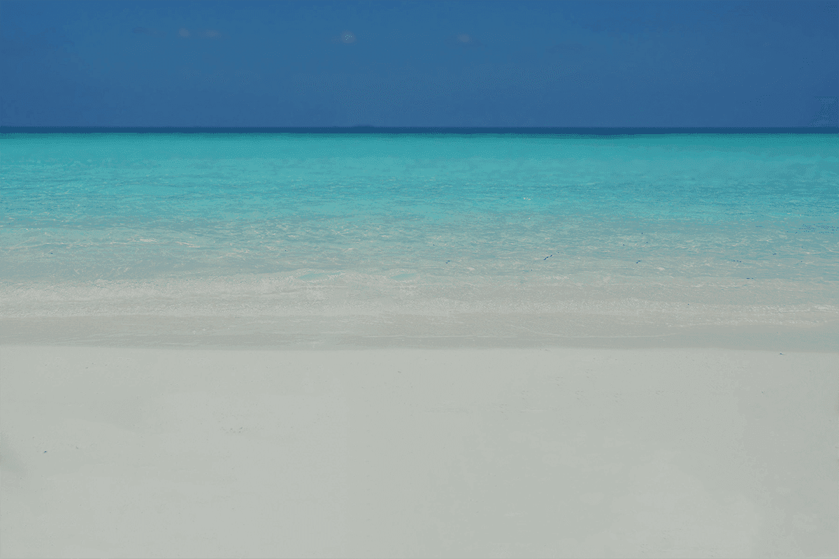 A photo of white sand beach, azure water and blue, clear horizon