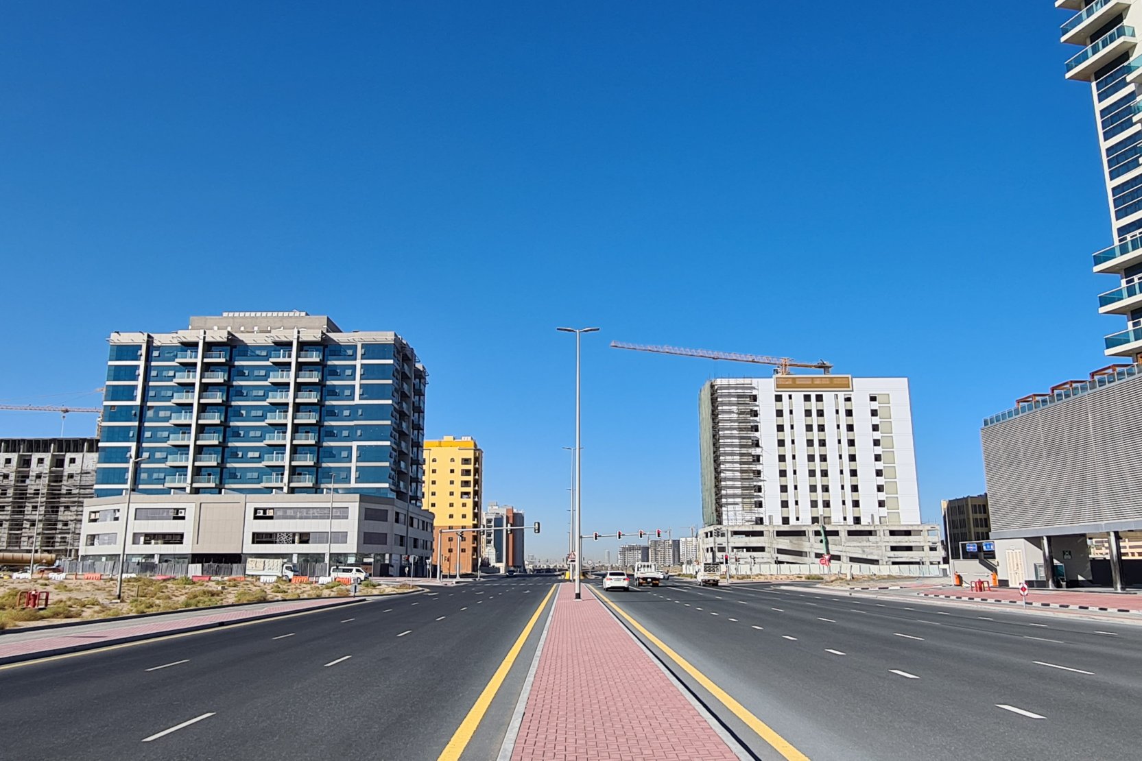 A wide, multi-lane road passing through the developing Majan community with high-rise buildings and construction.