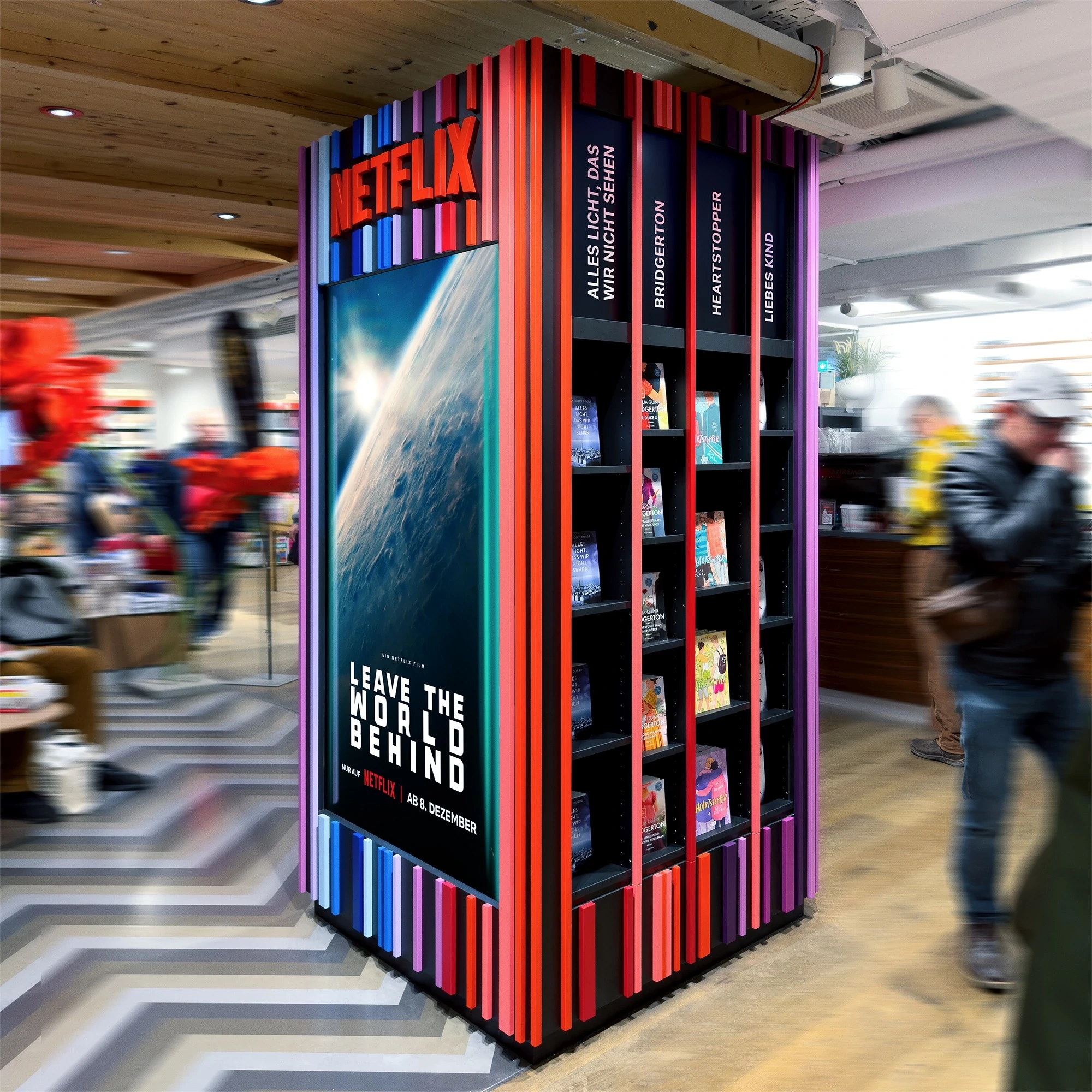 Free-standing NETFLIX TOWER in a bookstore with striped colorful corners, a large Leave The World Behind film poster and book shelves with series titles.