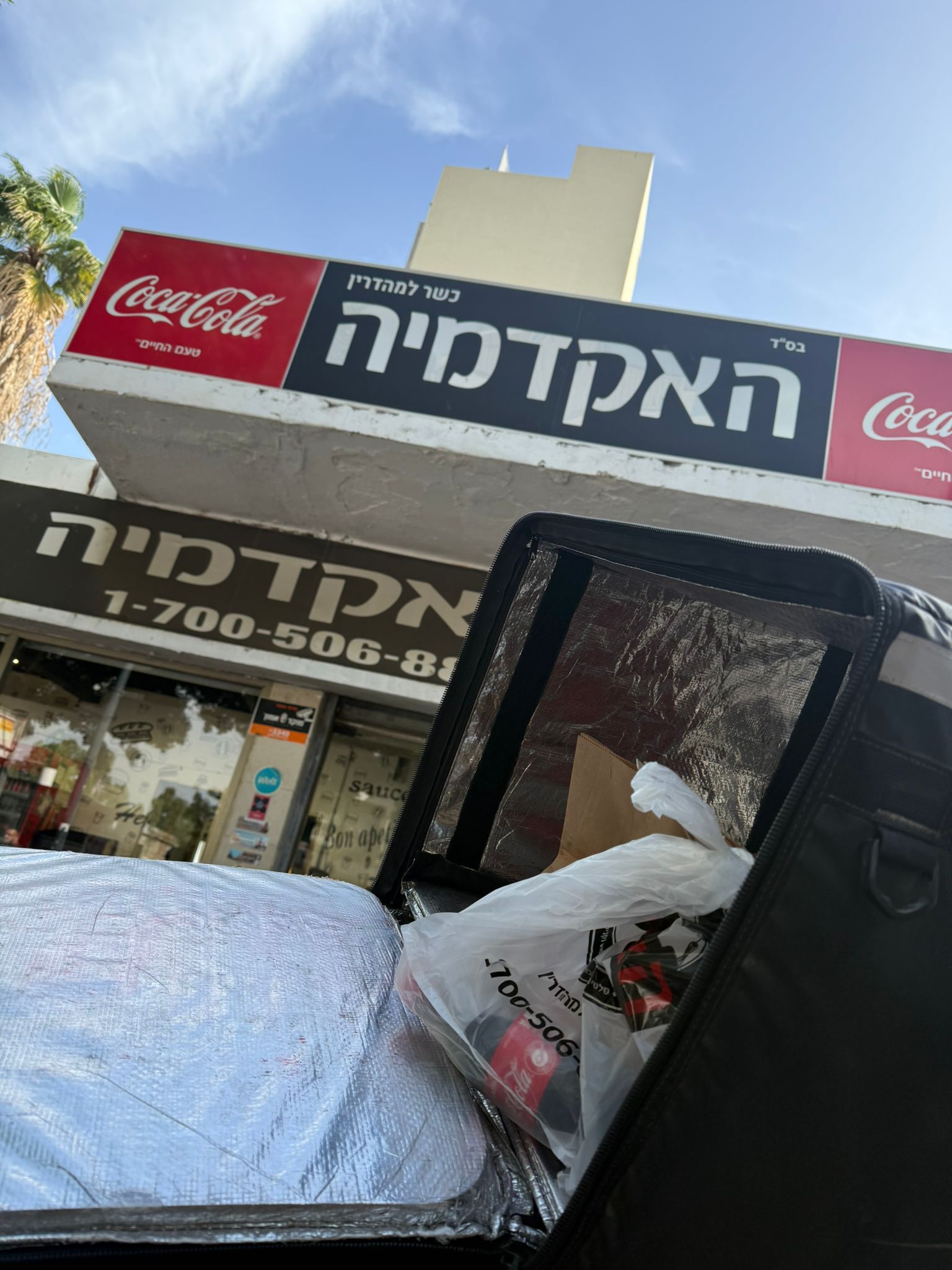 תיק משלוחים תרמי פתוח עם שקיות, מול שלט מסעדה.