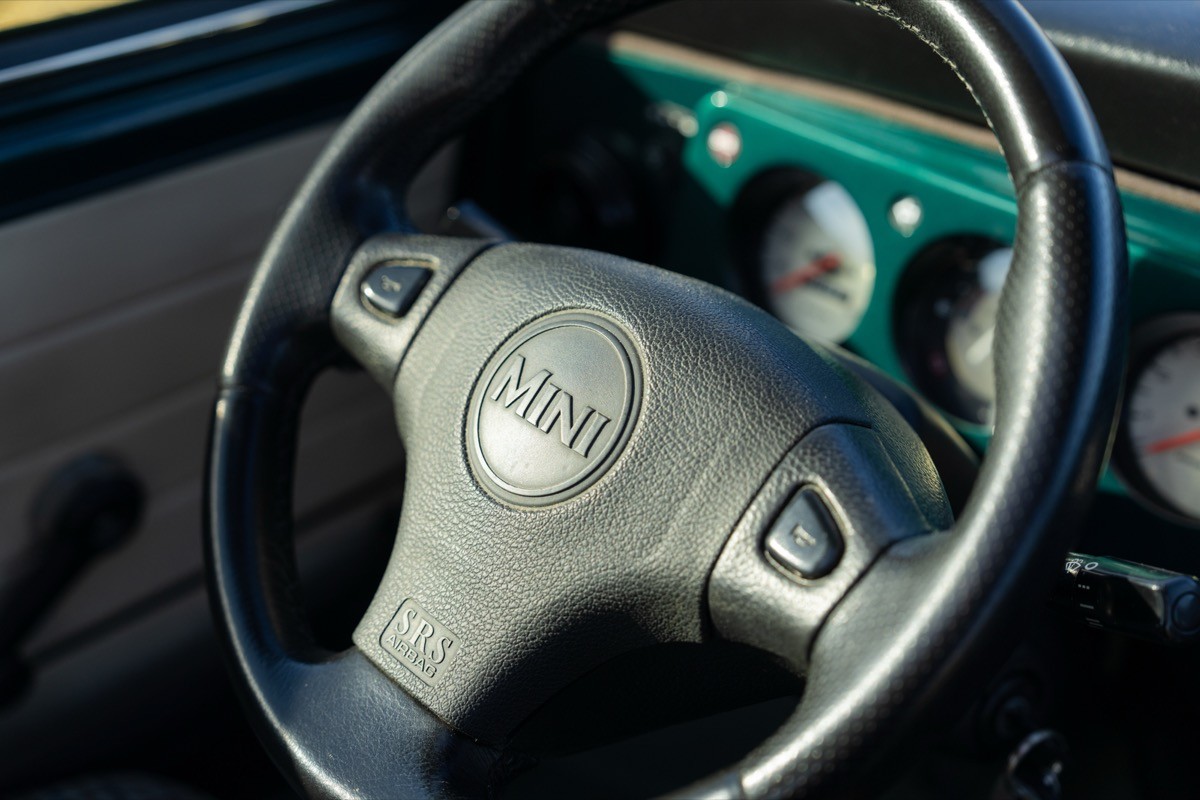 Close-up of a car steering wheel with black leather and a teal dashboard in the background.
