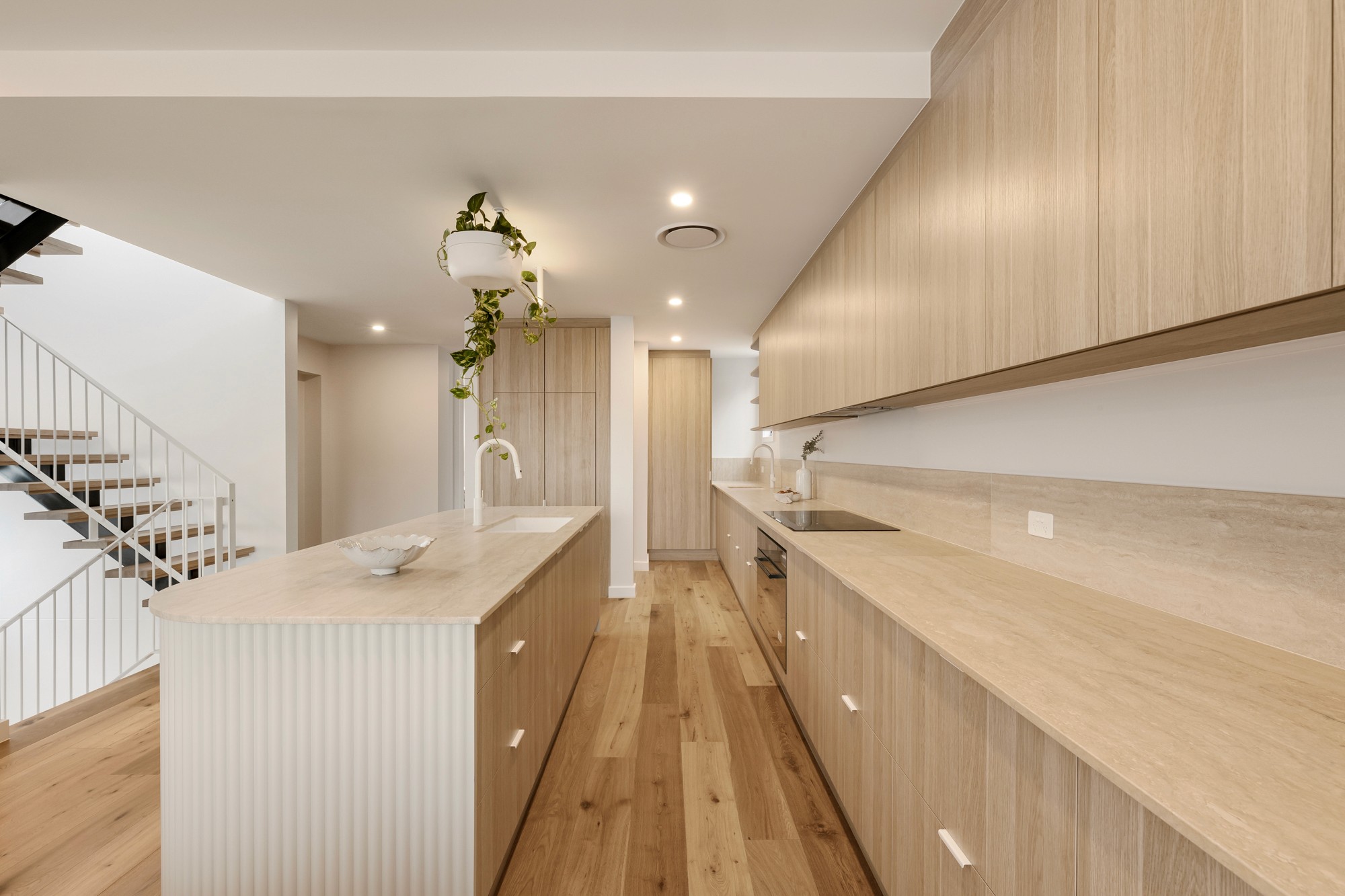 Kitchen with a curved stone island, long timber joinery and integrated lighting.