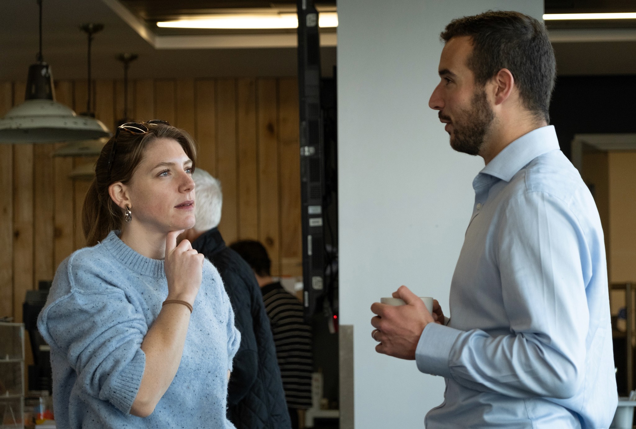 Two people interacting indoors, one wearing a blue sweater and the other in neutral clothes.
