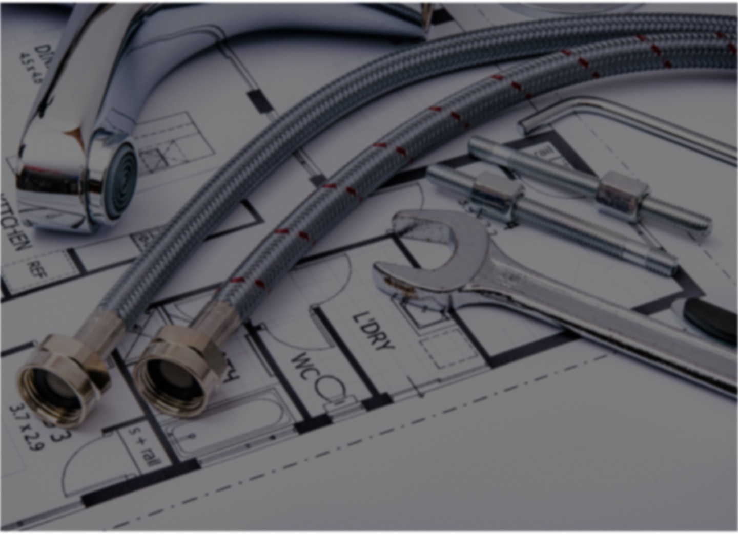 Plumbing tools, including a wrench and flexible hoses, placed on top of a detailed floor plan for a building project.