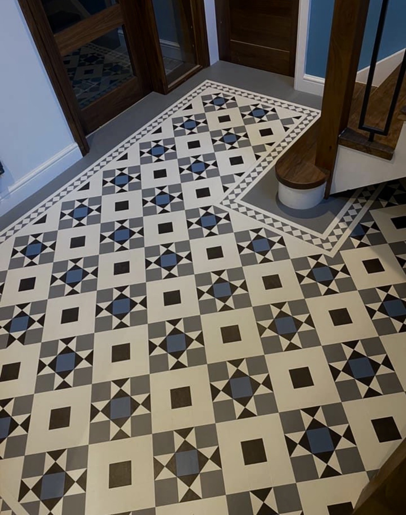 A smiling woman with her arms crossed, standing against a dark green background. She has long, dark hair.