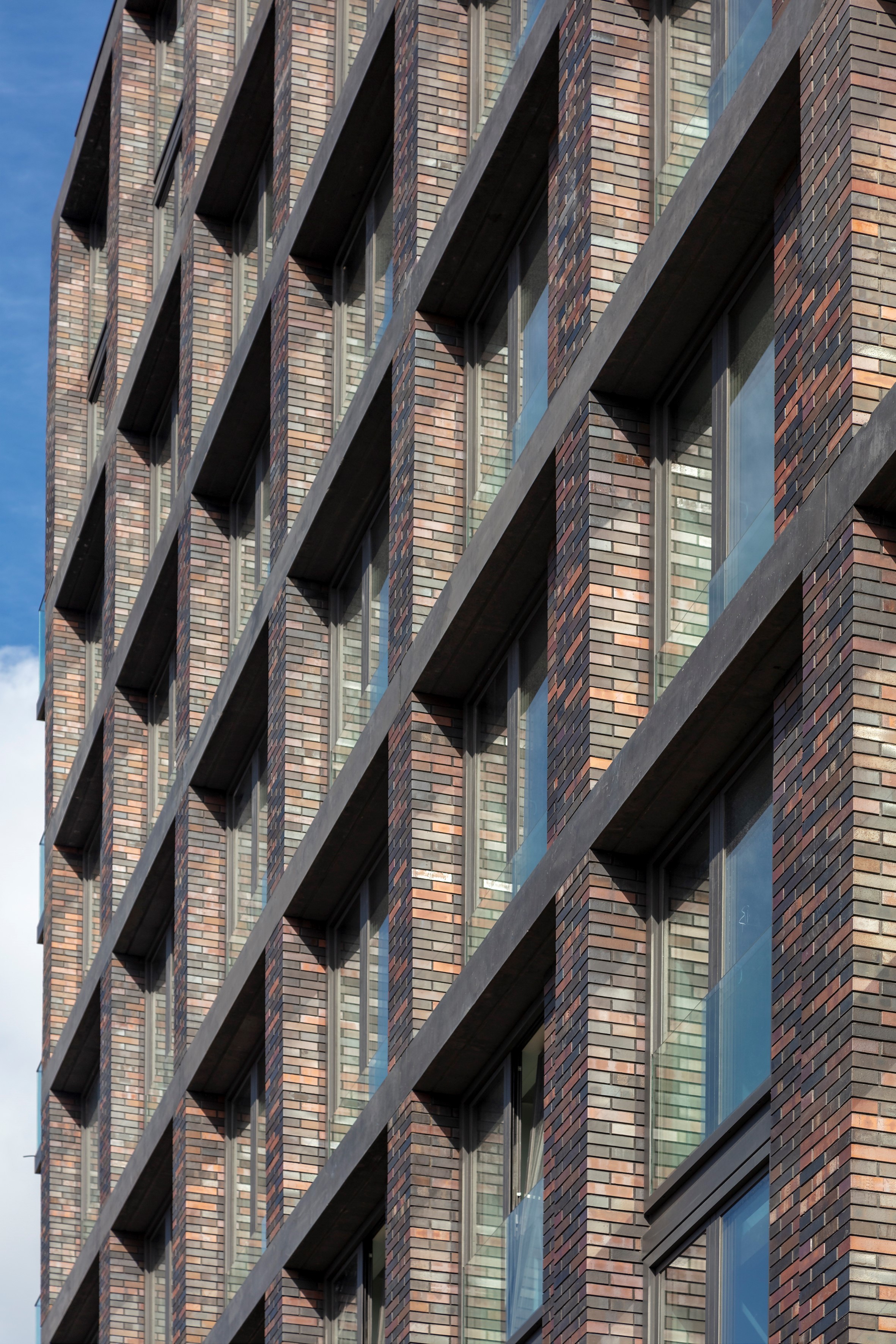Gelaagde bakstenen gevel van een gebouw met reflecterende glazen ramen en