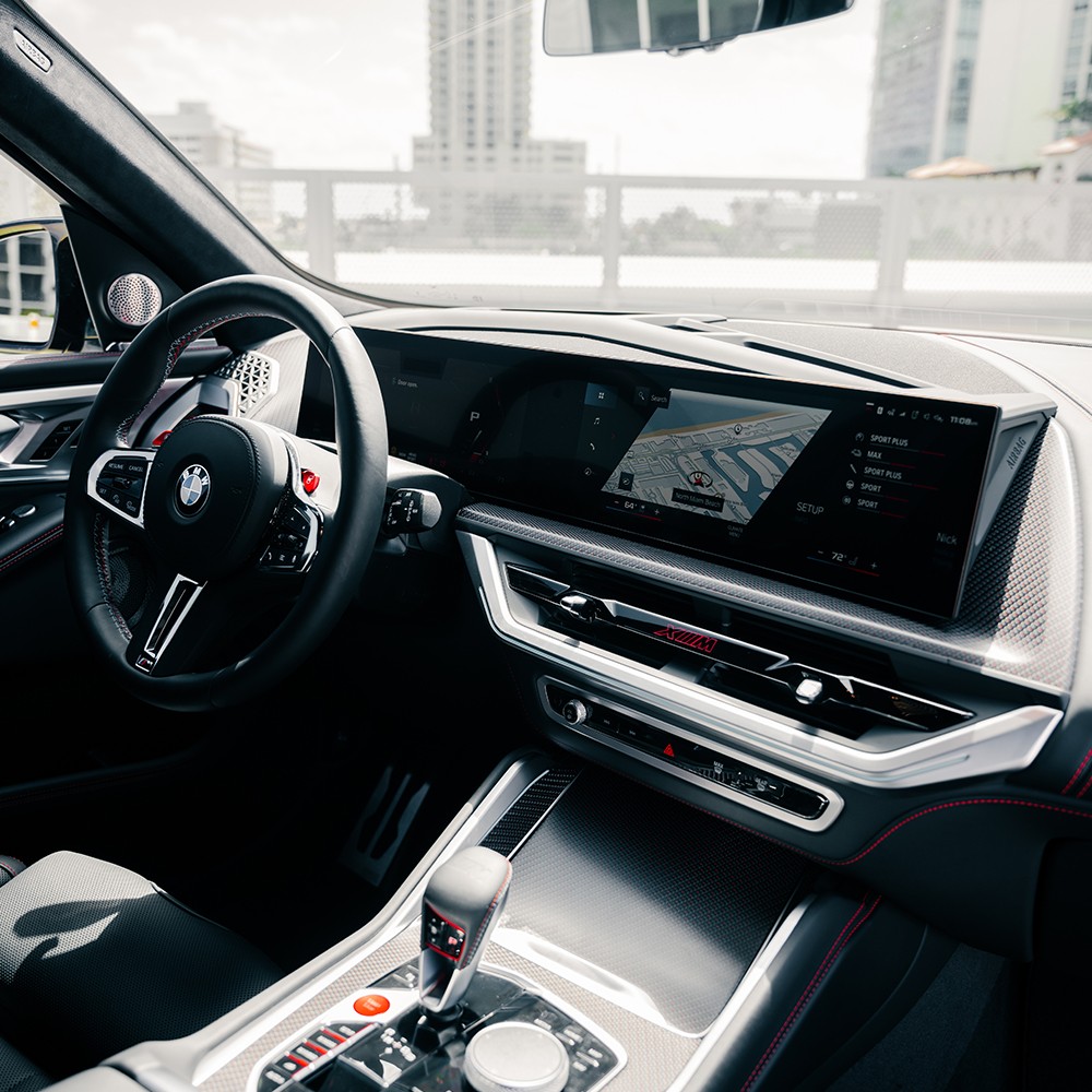 Driver's cockpit of the red BMW XM, featuring the large BMW Curved Display and M-specific controls.