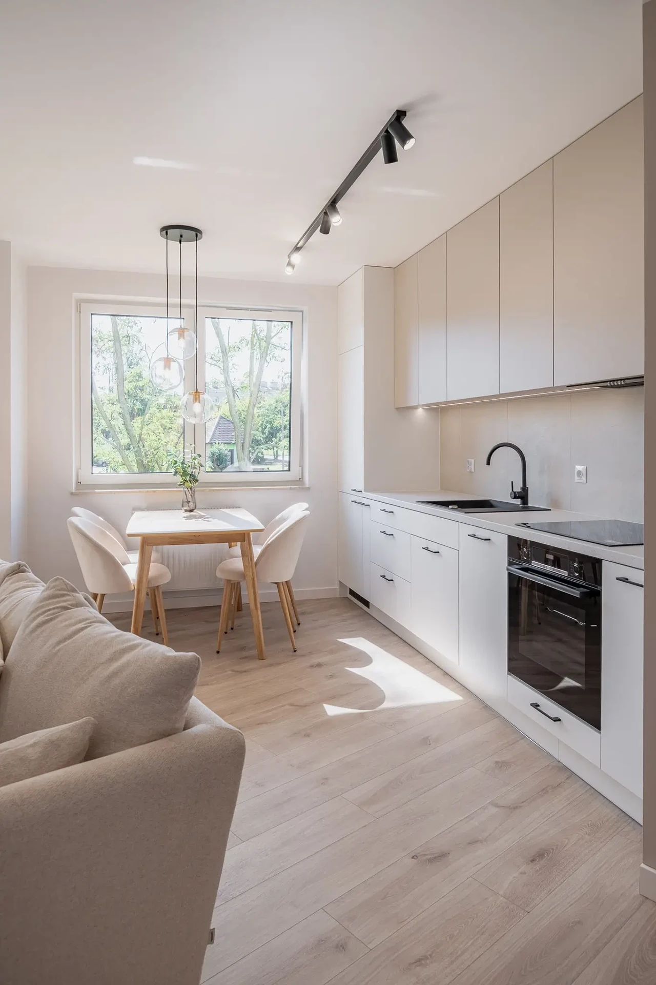 Beżowa kuchnia z wysoką zabudową i stołem jadalnianym w słonecznym salonie.