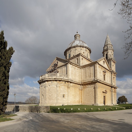 一座歷史悠久的石頭教堂，擁有高塔和圓頂，坐落在一片草坪上，天空部分多雲。