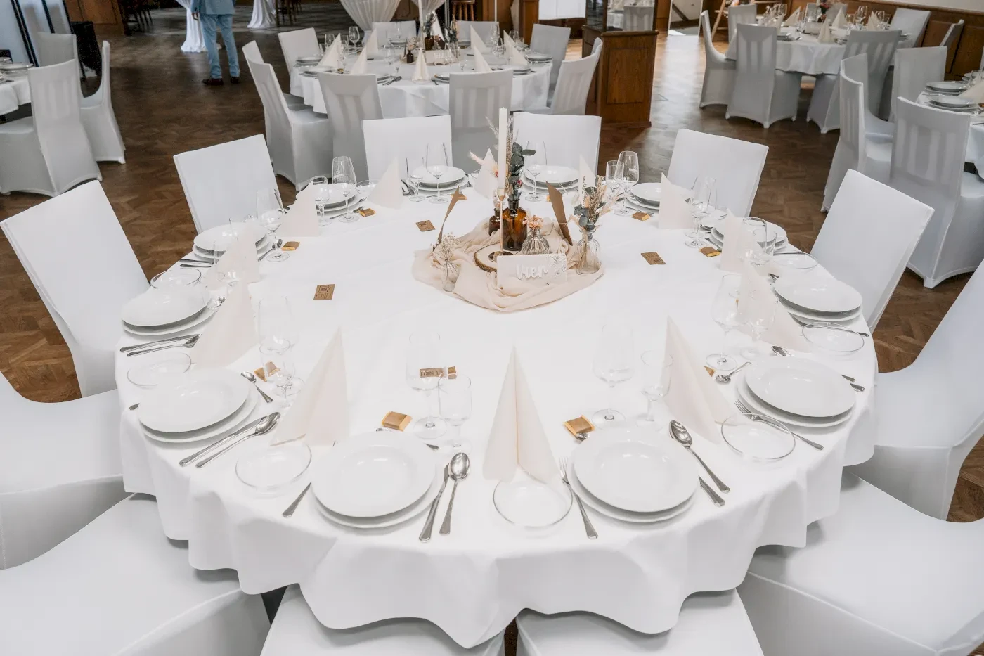 Ein runder Tisch mit weißer Tischdecke, Geschirr und Servietten, bereit für eine Feier.
