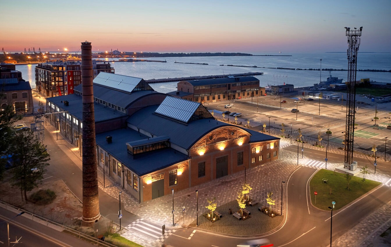 A building with a chimney and a street in front of the water
Description automatically generated