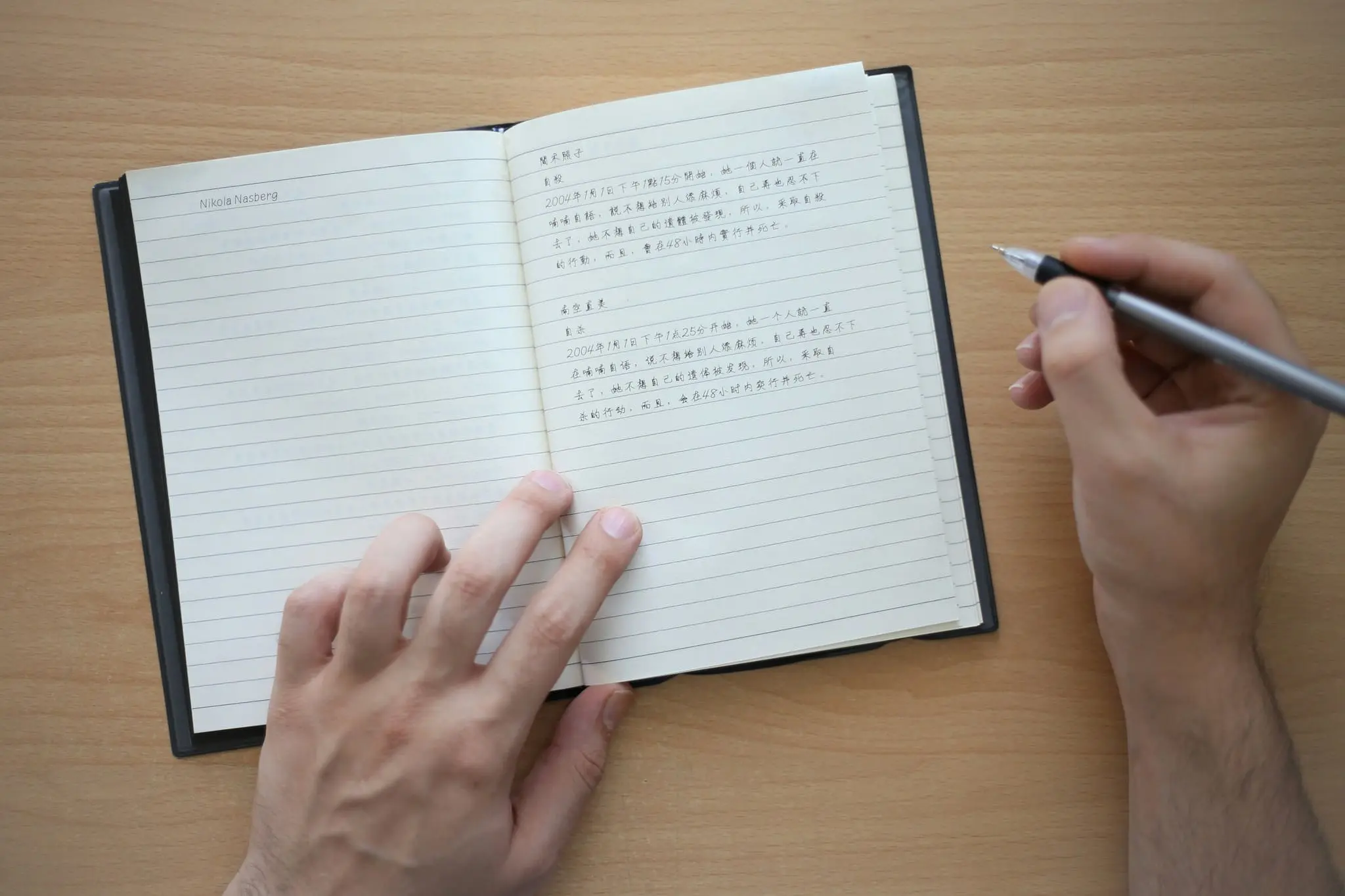 Hands holding a pen over an open notebook on a wooden desk.