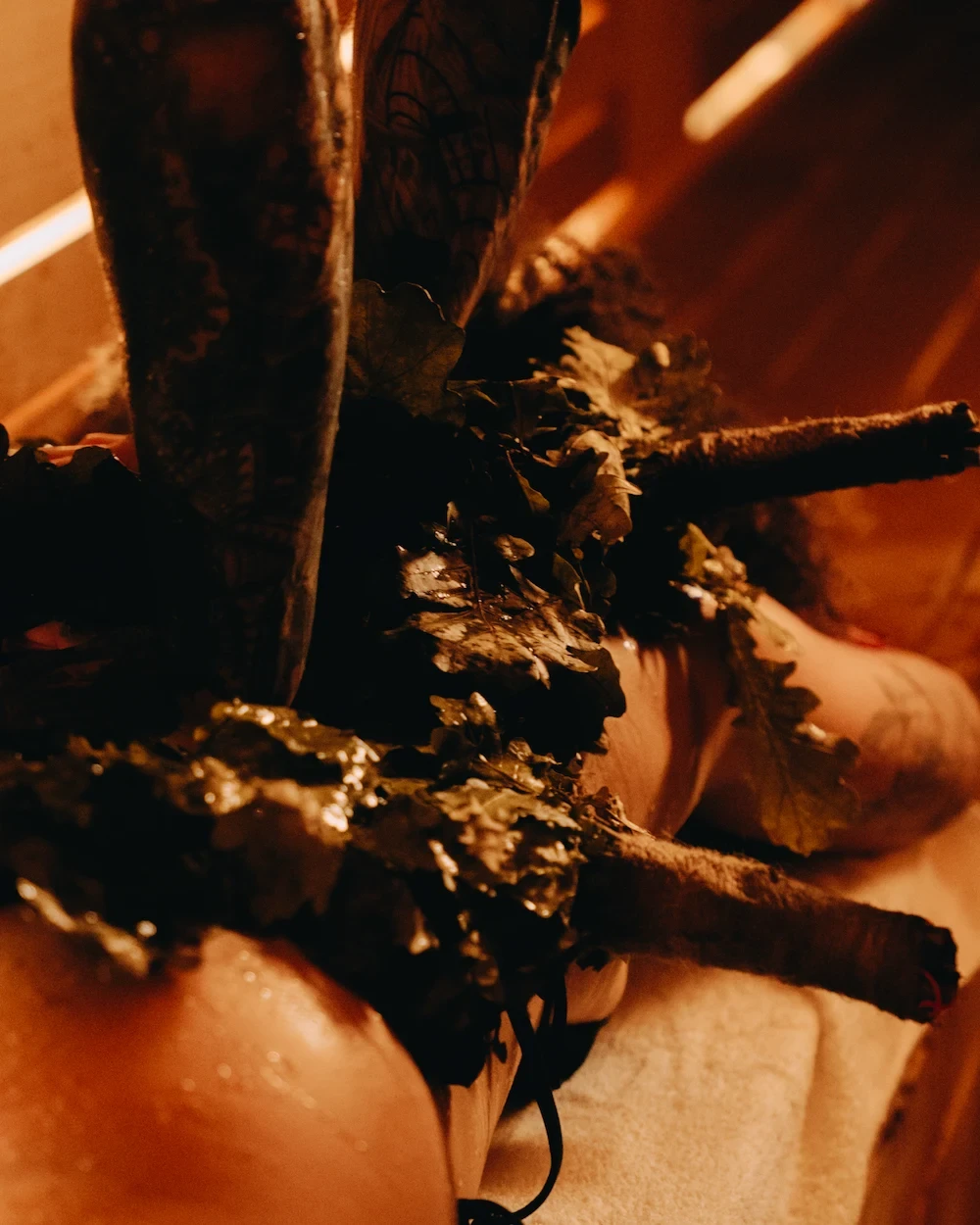 Traditional venik treatment during a Russian-inspired sauna ritual using leafy branches and steam.