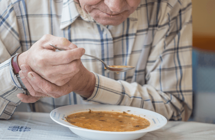 Elderly person eating soup with spoon, close-up.