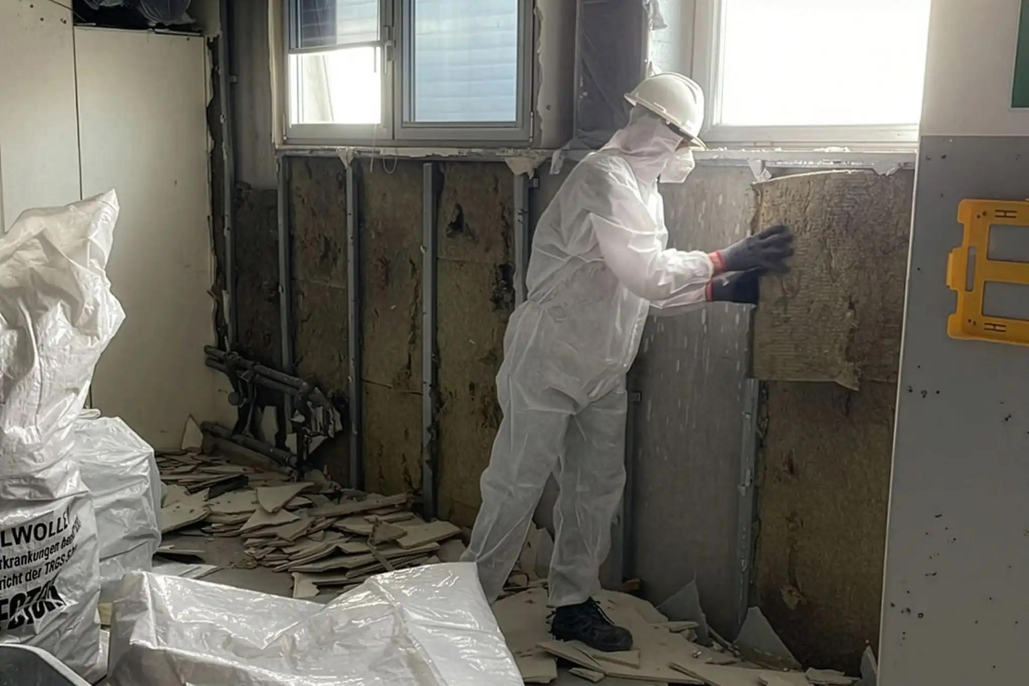 Arbeiter in Schutzanzug bei Schadstoffsanierung beim Entfernen von Mineralwolle im Innenbereich