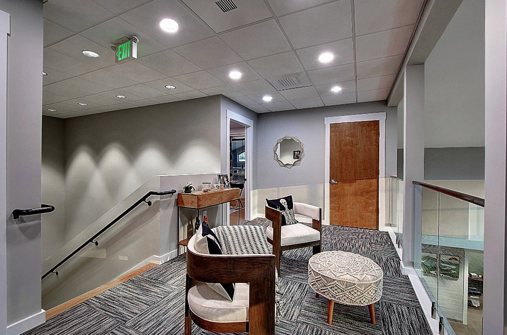Bright, modern interior featuring a staircase, seating area, and decorative wall art. Warm lighting enhances the space.