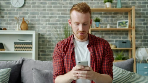 Young man in a cozy living room looking calmly at his smartphone.