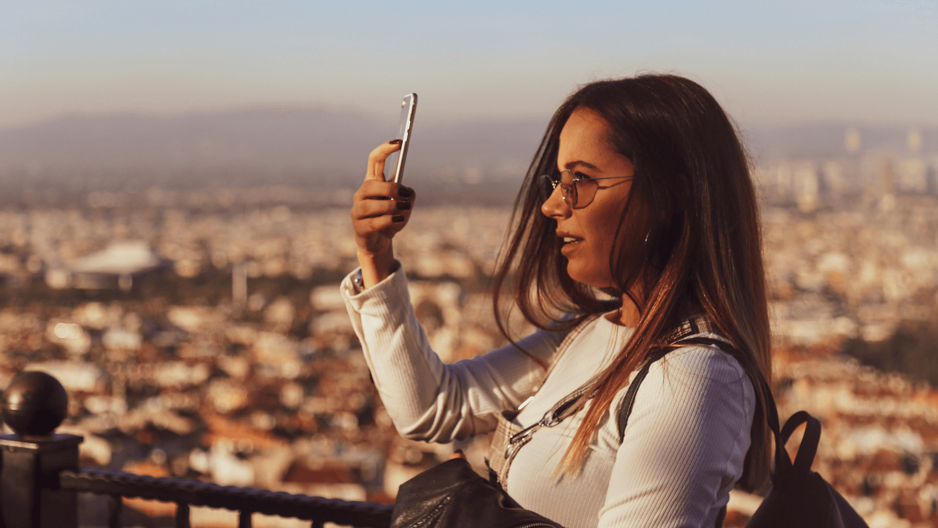A woman, side on, poses for a selfie in front of a city vista